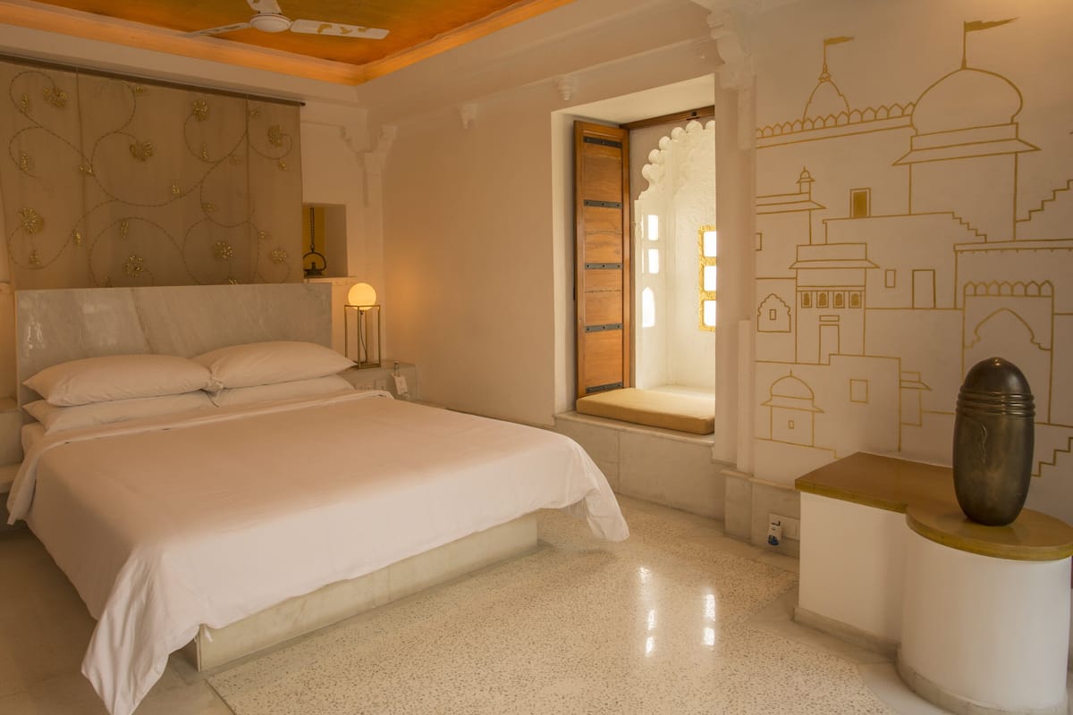 A bedroom with a large bed, two bedside lamps, a window with a view, and a decorative wall with architectural drawings.
