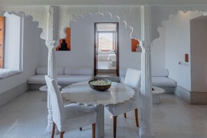 A room with a round table, white chairs, a white sofa, and a view of a mountainous landscape through an open doorway.