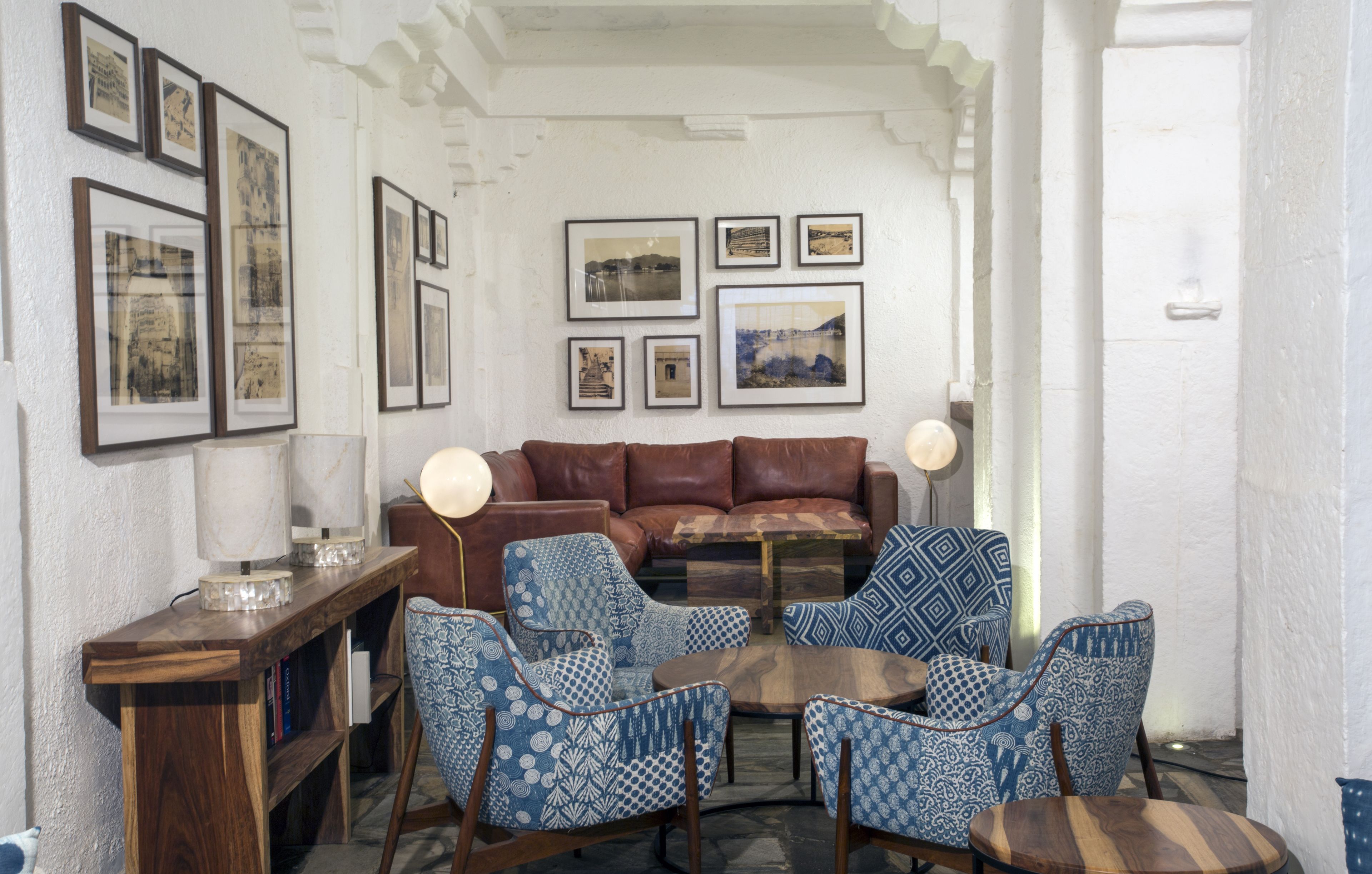 A living room with a brown leather sofa, patterned blue chairs, a wooden coffee table, and framed pictures on the wall.