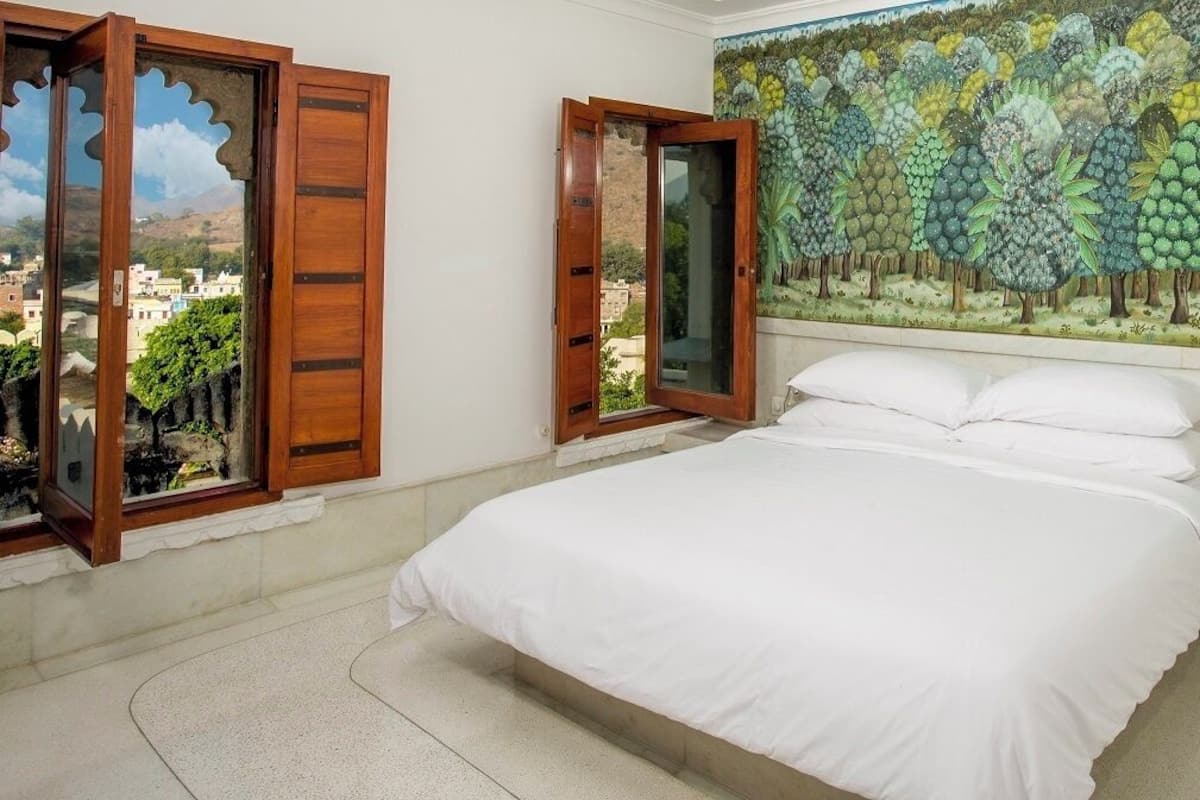 A bedroom with a bed, a view through a wooden door, and a mural of trees on the wall.