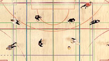 A basketball court with players in motion, wooden flooring, and colored boundary lines.
