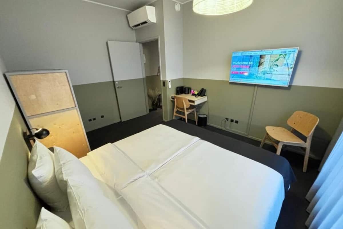 A hotel room with a bed, a desk, a chair, a television, and a wardrobe.