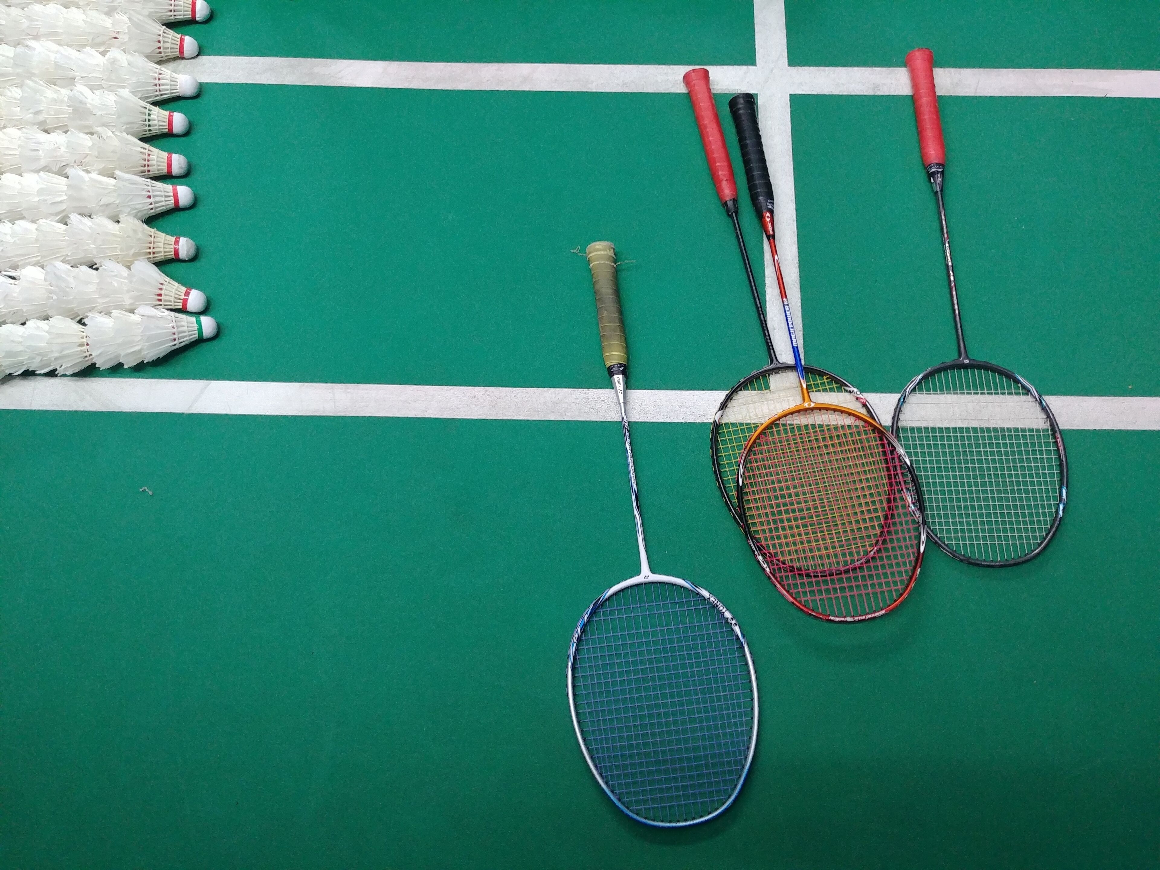 A green surface with white lines, possibly a sports court, and several badminton rackets and shuttlecocks arranged on it.