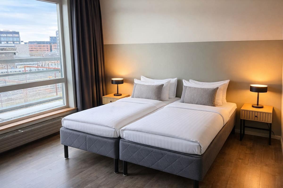 A double bed with two bedside tables, a window with a view of buildings, and a radiator.