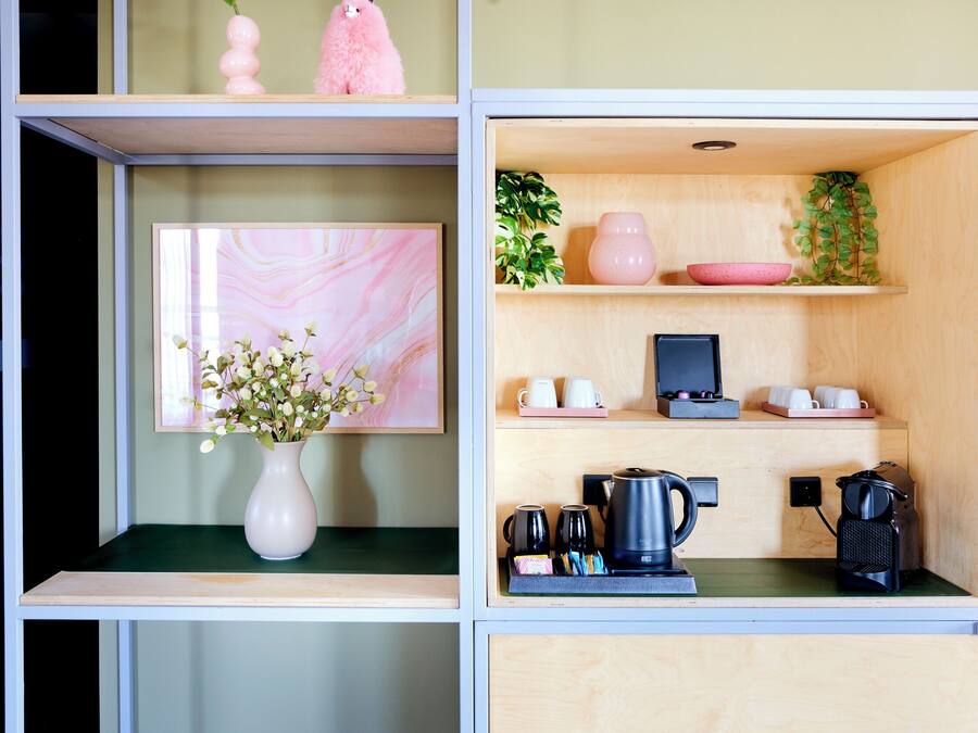 Un espacio habitable compacto con una estación de café, una obra de arte enmarcada y un jarrón rosa con flores.