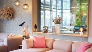 A modern living room with a sofa, a small table, a lamp, and a window with a view of greenery. - CPH Hotel (Copenhagen)