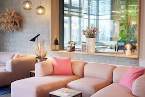A modern living room with a sofa, a small table, a lamp, and a window with a view of greenery. - CPH Hotel (Copenhagen)