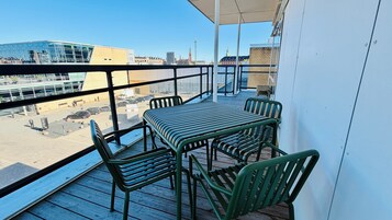 Un balcón con mesa y sillas, con vista a un paisaje urbano de edificios y cielo despejado.