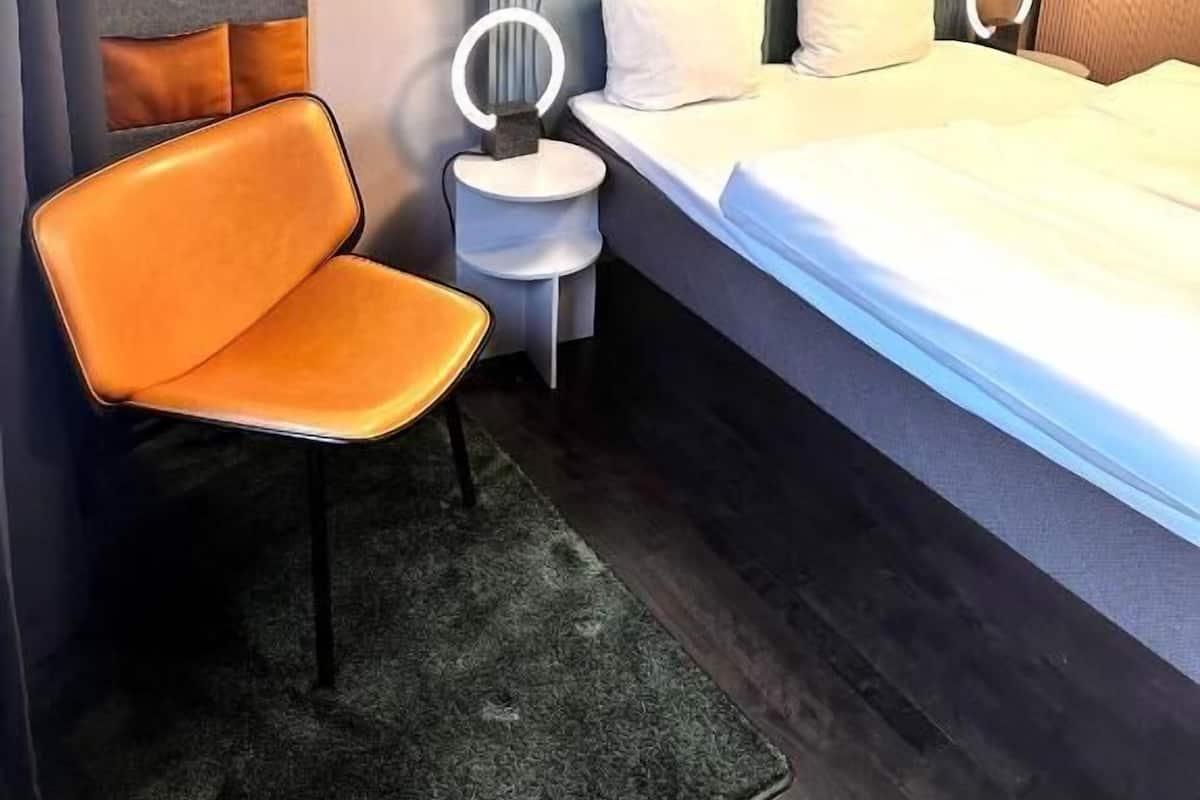 A modern hotel room with a bed, a chair, a bedside table, and a headboard with the word "HELLO" on it.