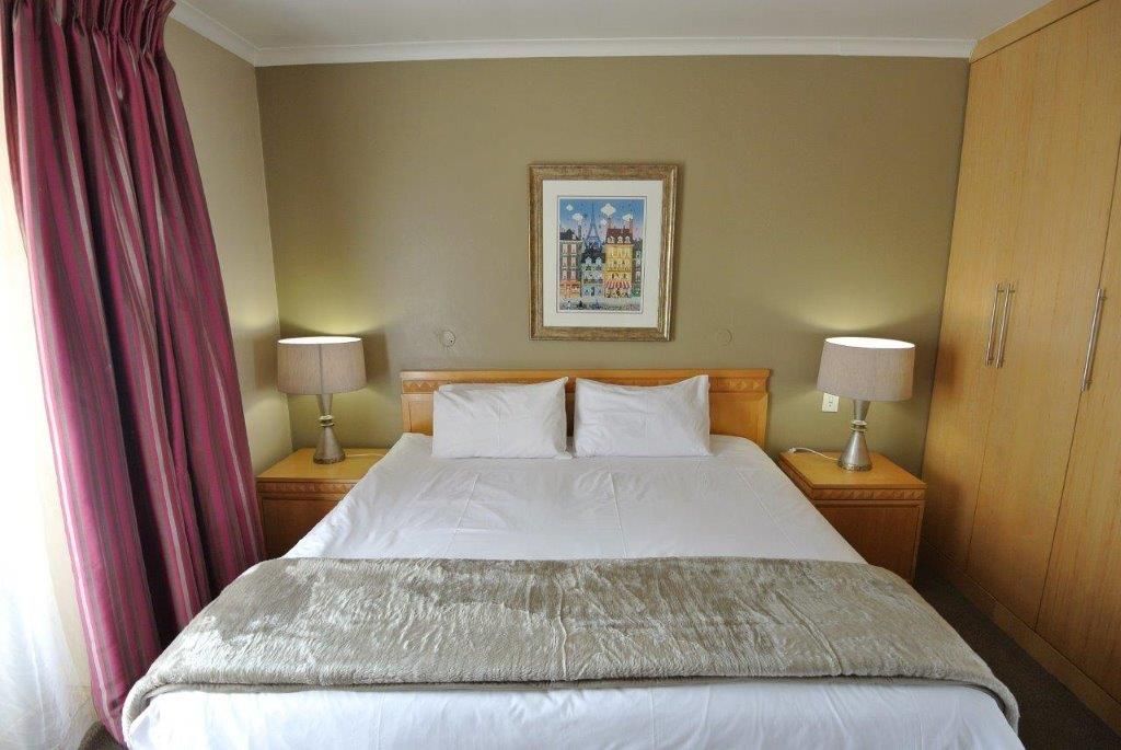 A hotel room with a bed, two bedside tables with lamps, a large painting on the wall, and a wardrobe.