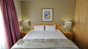 A hotel room with a bed, two bedside tables with lamps, a large painting on the wall, and a wardrobe.