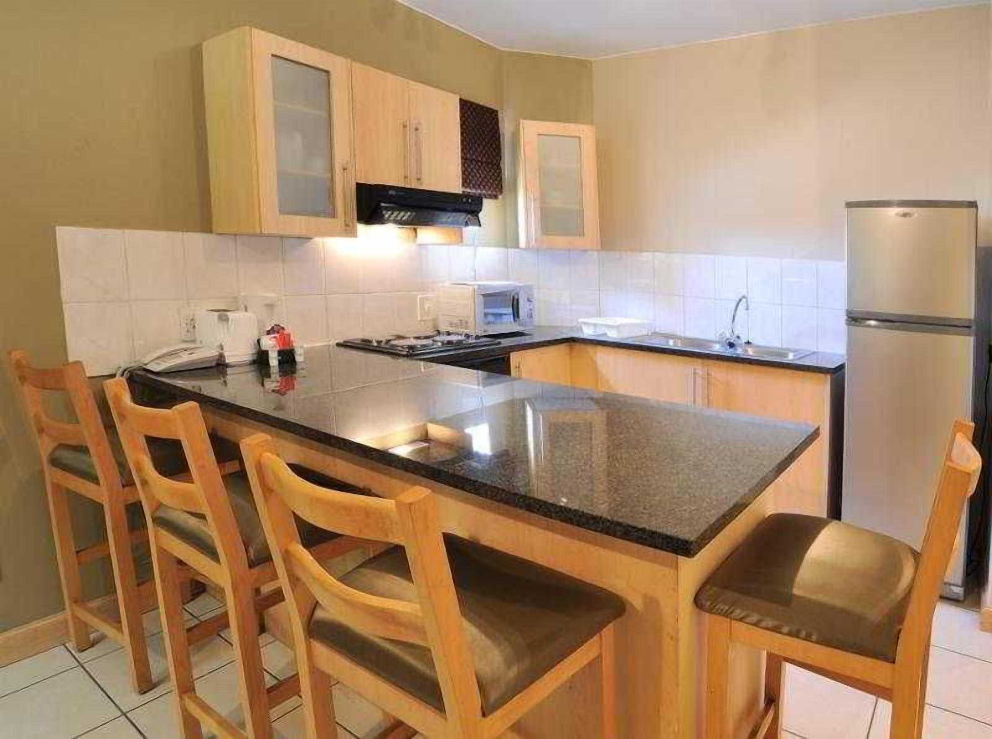 A kitchen with a central island, wooden chairs, a refrigerator, and a microwave.