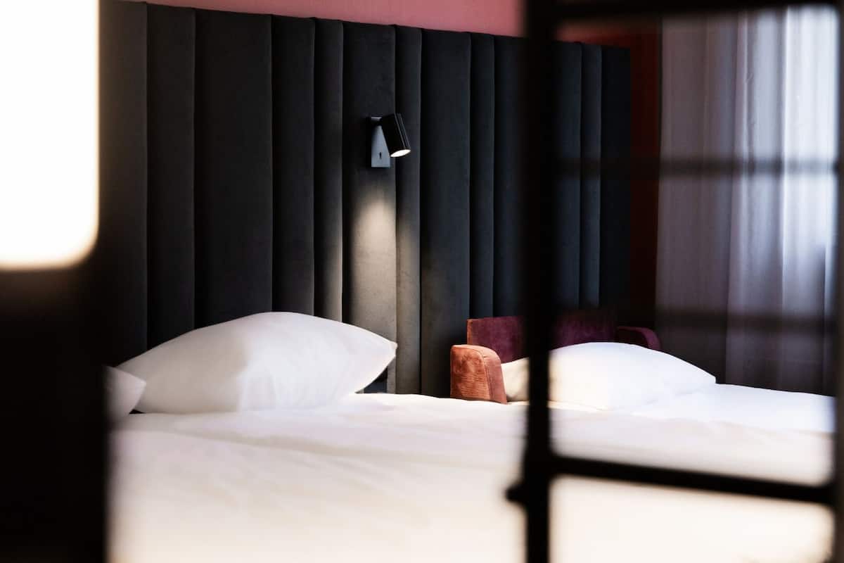 A hotel room with a bed, a nightstand, and a wall-mounted lamp.