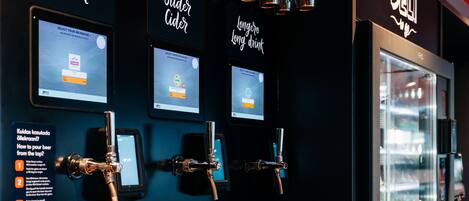 Zona de bar con grifos múltiples y pantallas mostrando opciones de bebidas.