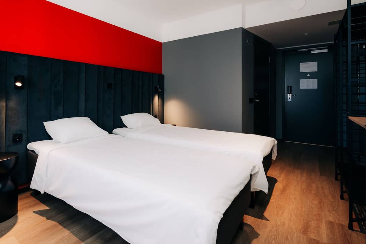 A modern hotel room with two beds, a desk, and a chair.