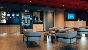 Un moderno vestíbulo de hotel con asientos, un minibar, una cafetera y una pantalla digital que muestra 'Tallink Hotels Express'.
