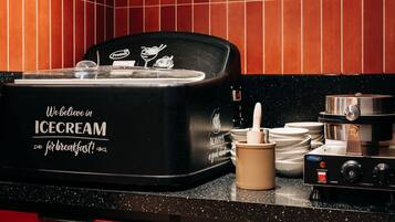 Una macchina per gelati nera con uno slogan, una moka e un set di piatti bianchi su un bancone da cucina.