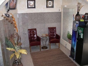 Una habitación con dos sillones de cuero, una mesita, una planta decorativa y un refrigerador.