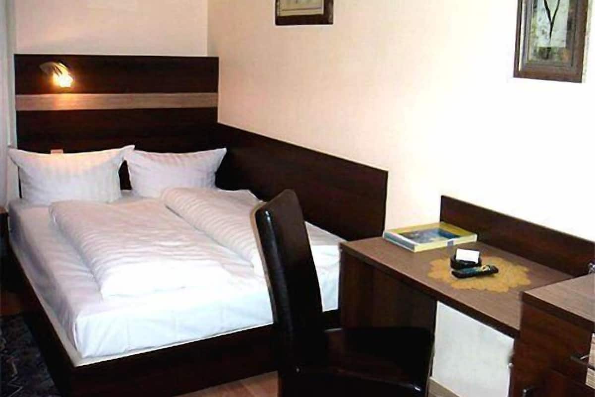 A hotel room with a bed, a desk, and a chair. There are two paintings on the wall.