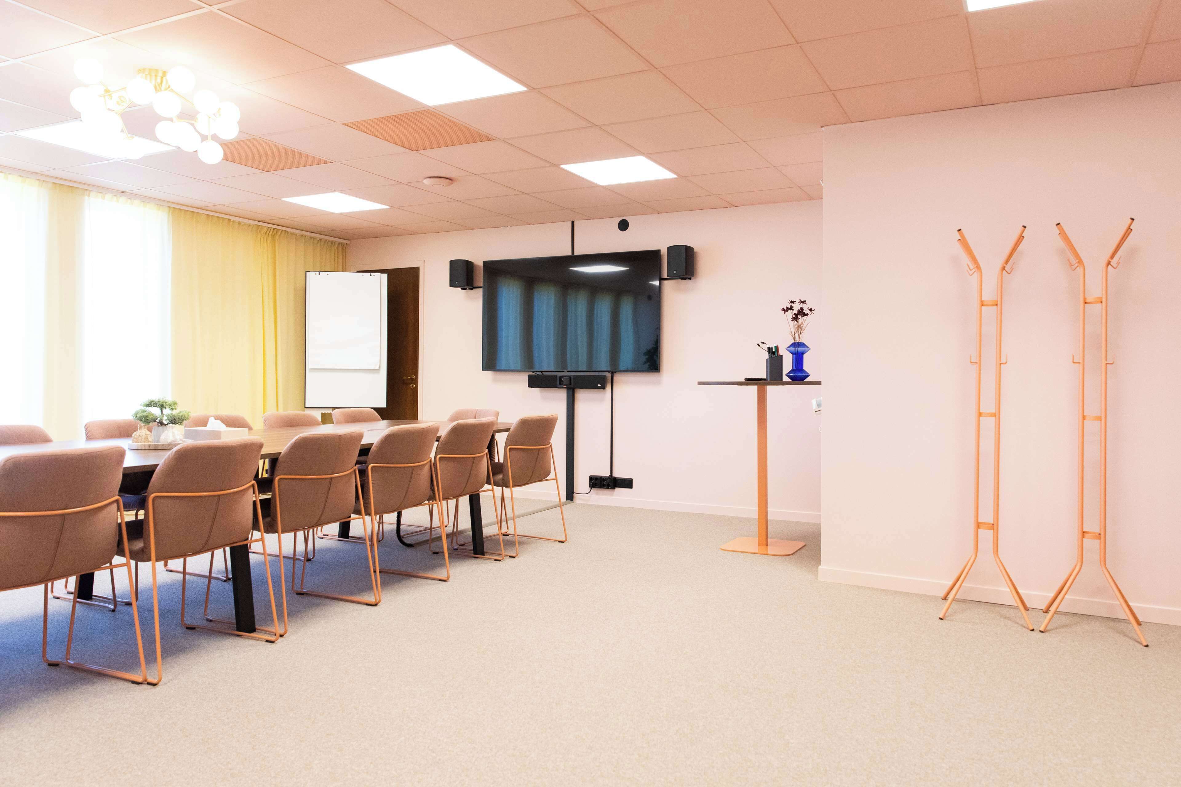 A conference room with a whiteboard, a flat-screen TV, a table with chairs, and a stand with a vase.
