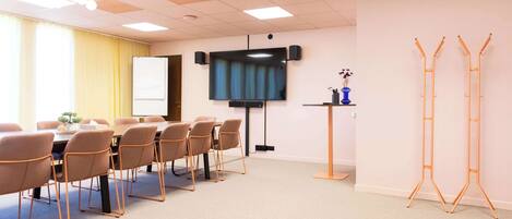 Una sala de conferencias con una pizarra, un televisor de pantalla plana, una mesa con sillas y un atril con un jarrón.