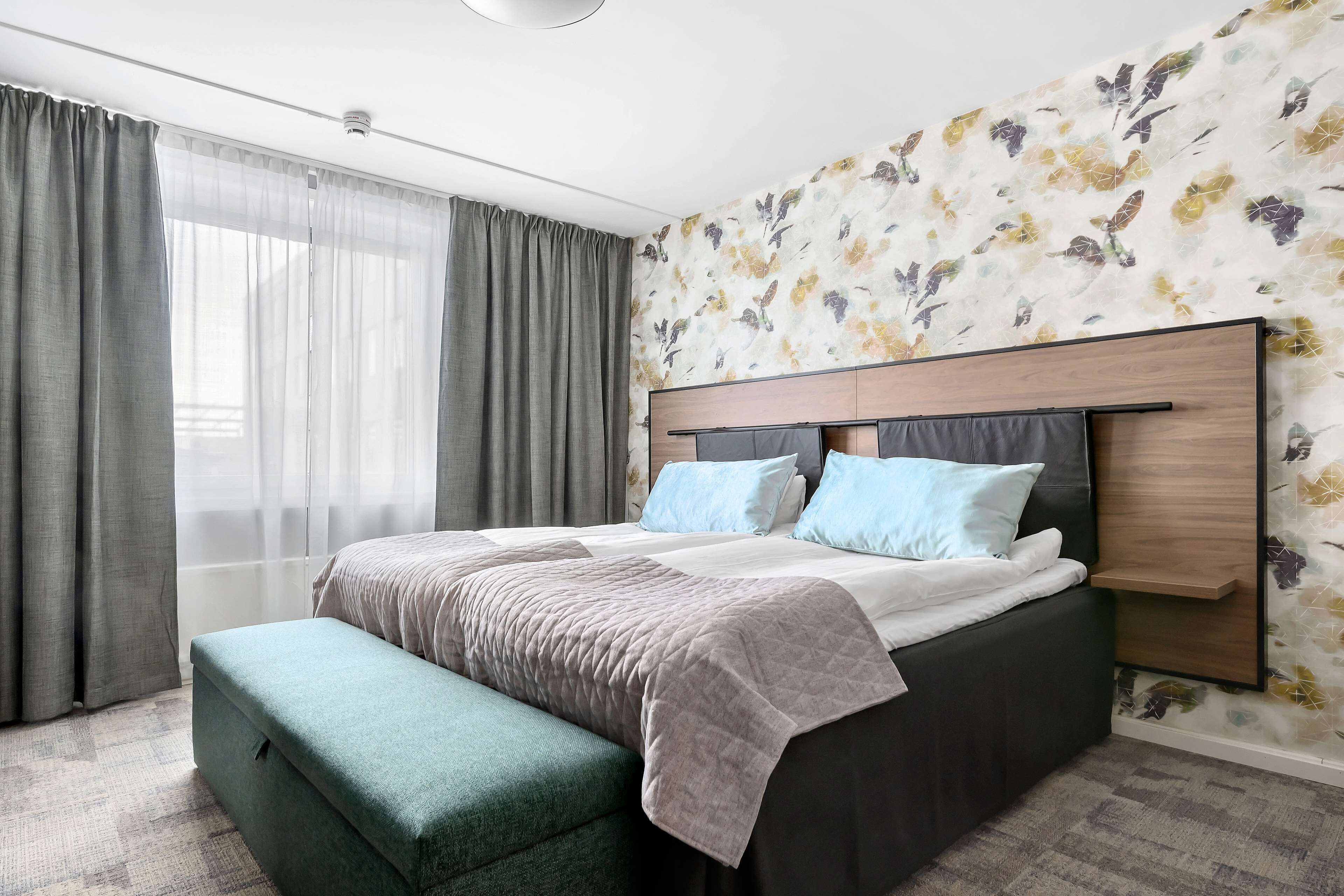 Ein modernes Hotelzimmer mit einem großen Bett, einem hölzernen Kopfteil und einer grünen Bank.