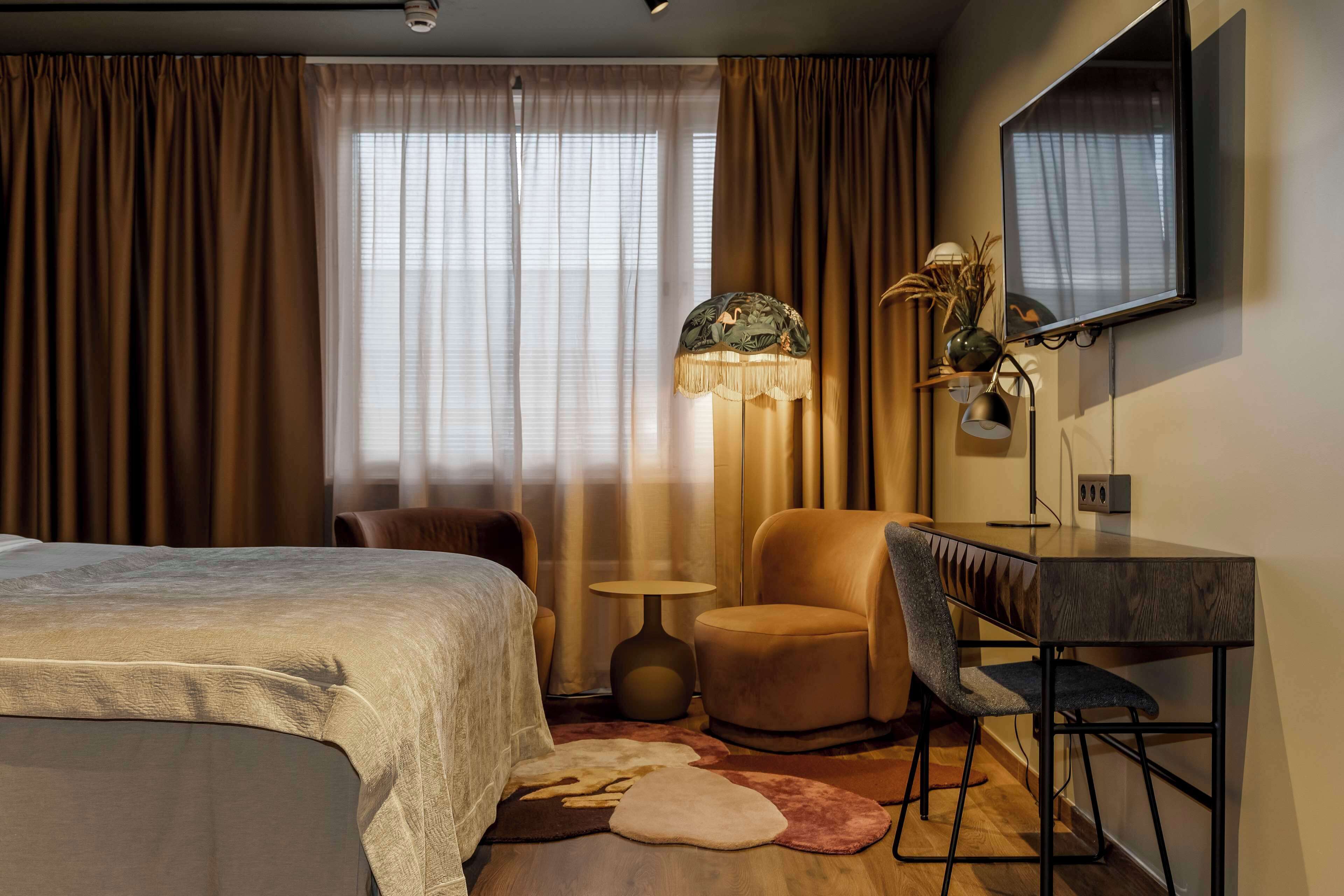 Una habitación de hotel moderna con una cama, dos sillas, un escritorio, una lámpara y un televisor montado en la pared.