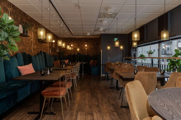 A restaurant with wooden flooring, cushioned seating, pendant lighting, and a view of the city through large windows.