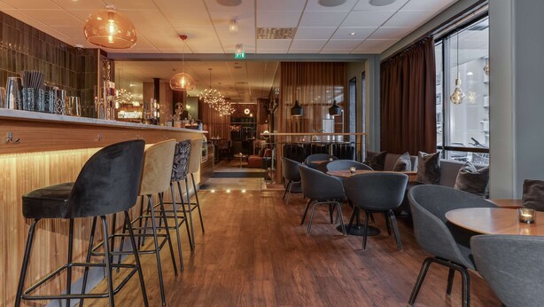 A modern bar area with wooden flooring, bar stools, and pendant lighting.