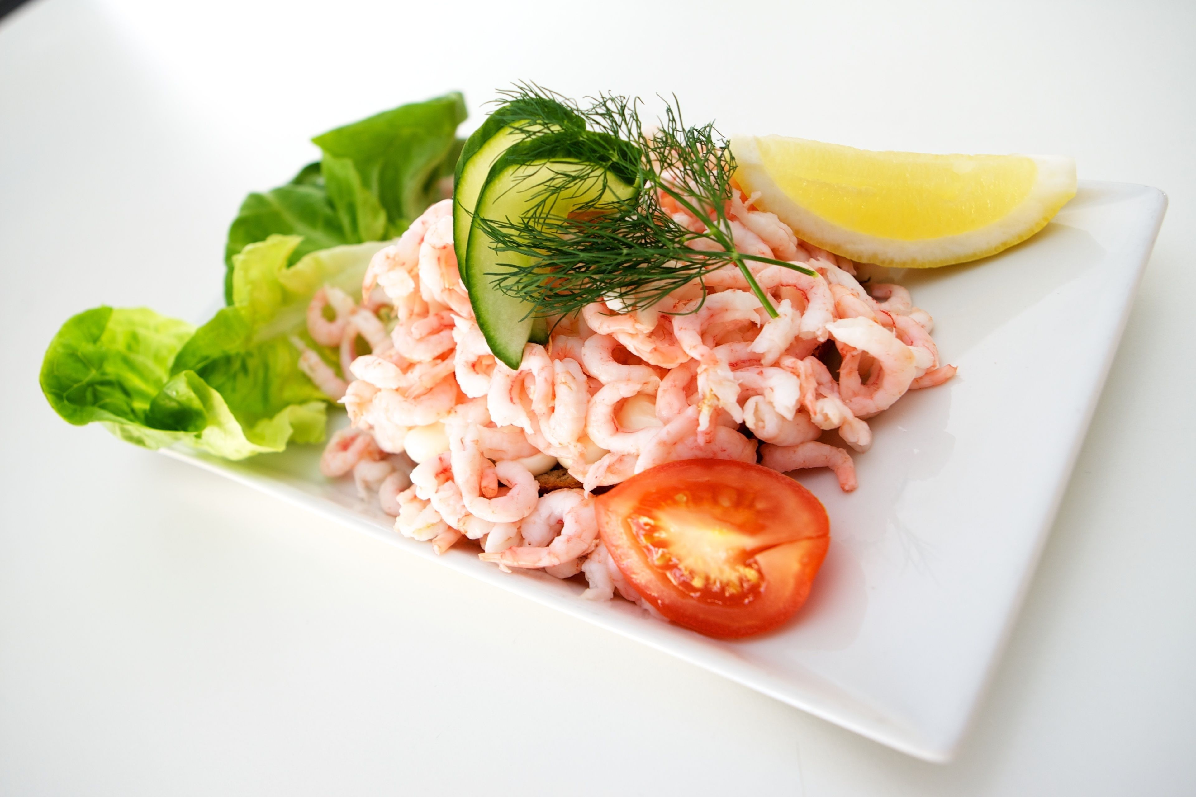 Un plato de ensalada de camarones con lechuga, pepino, eneldo y limón.
