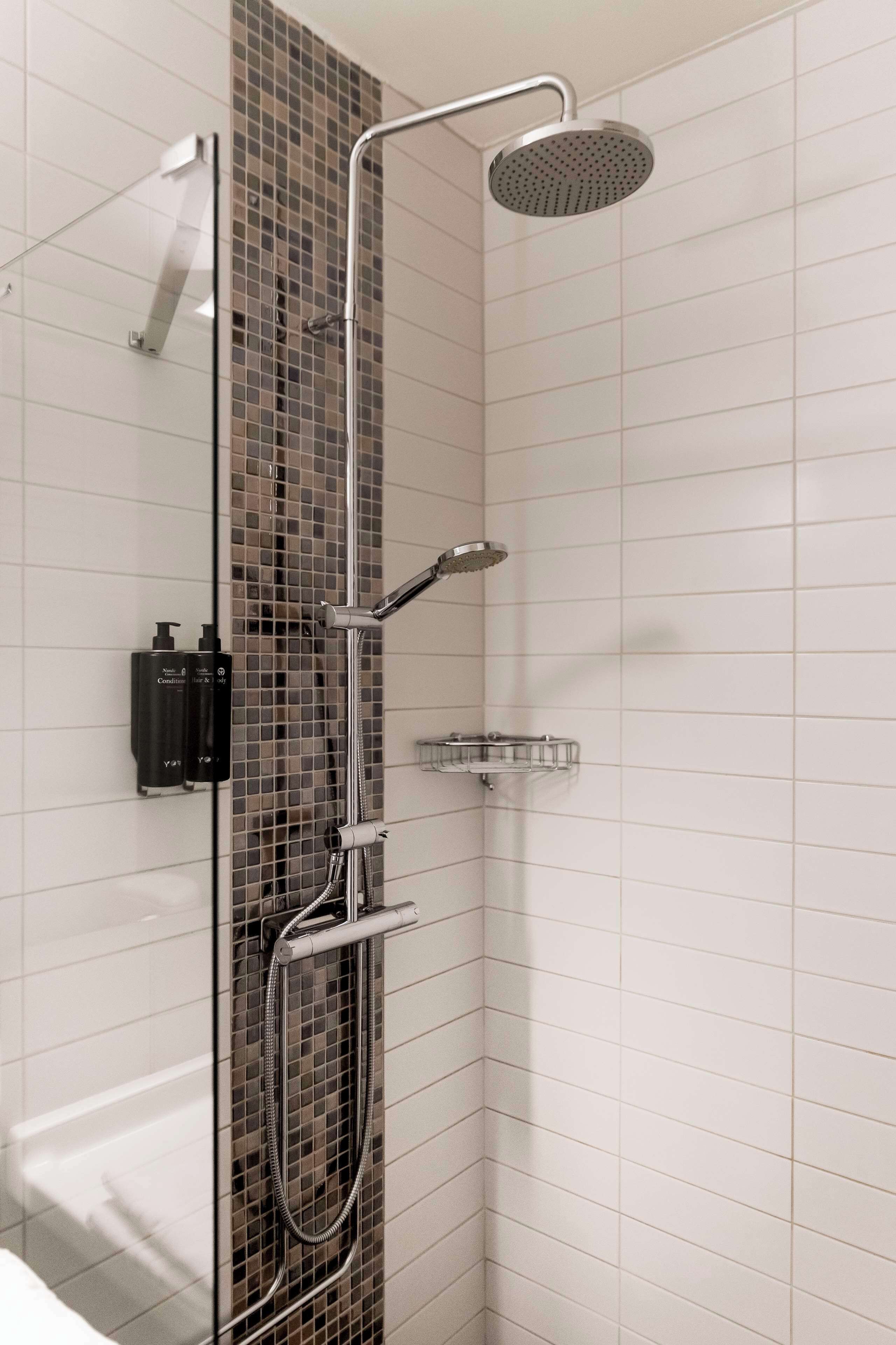 Une douche moderne dotée d’un pommeau de douche à pluie, d’un pommeau de douche à main et d’un flexible de douche à main.
