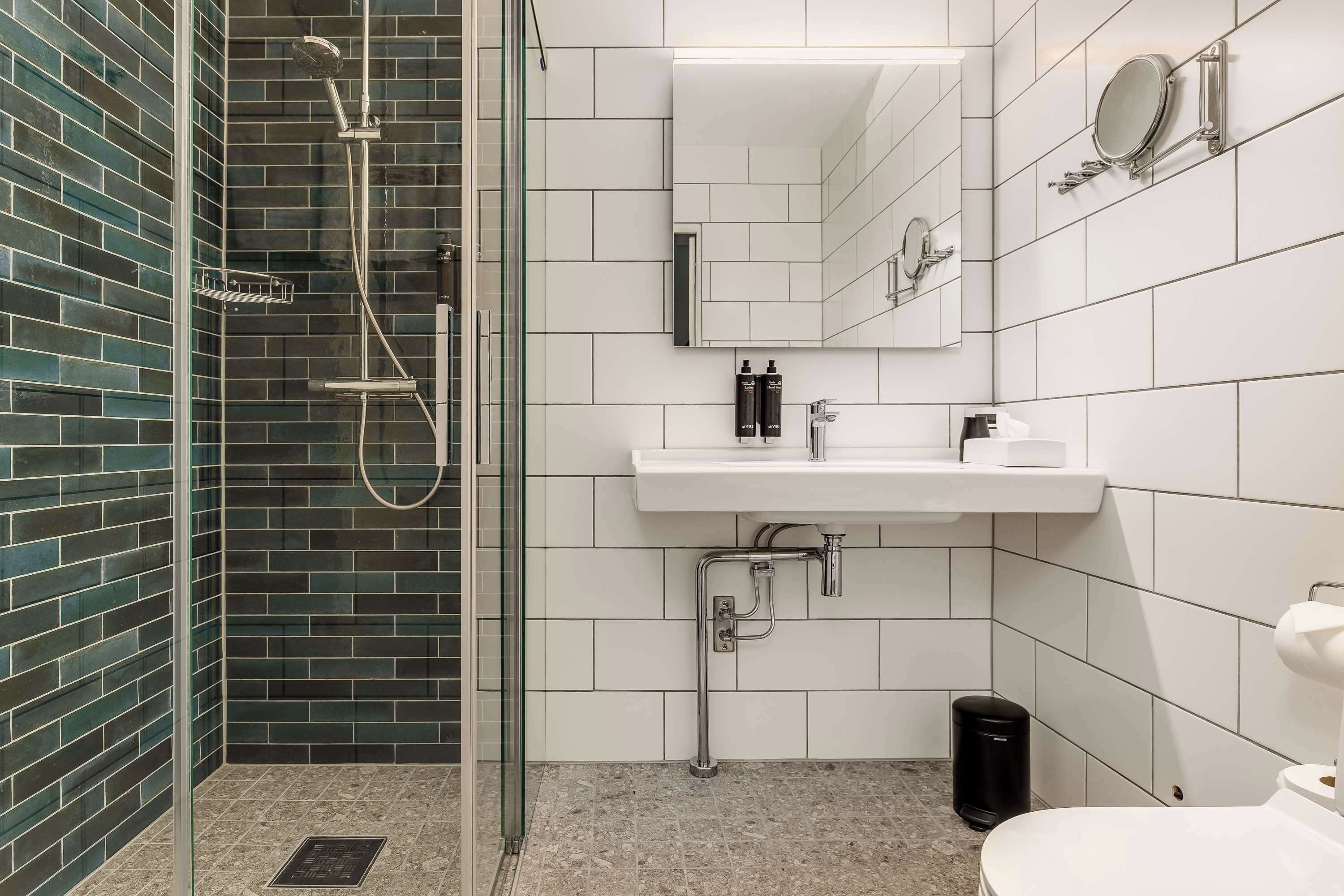 A modern bathroom with a glass-enclosed shower, white tiles, a sink with a mirror, and a toilet.