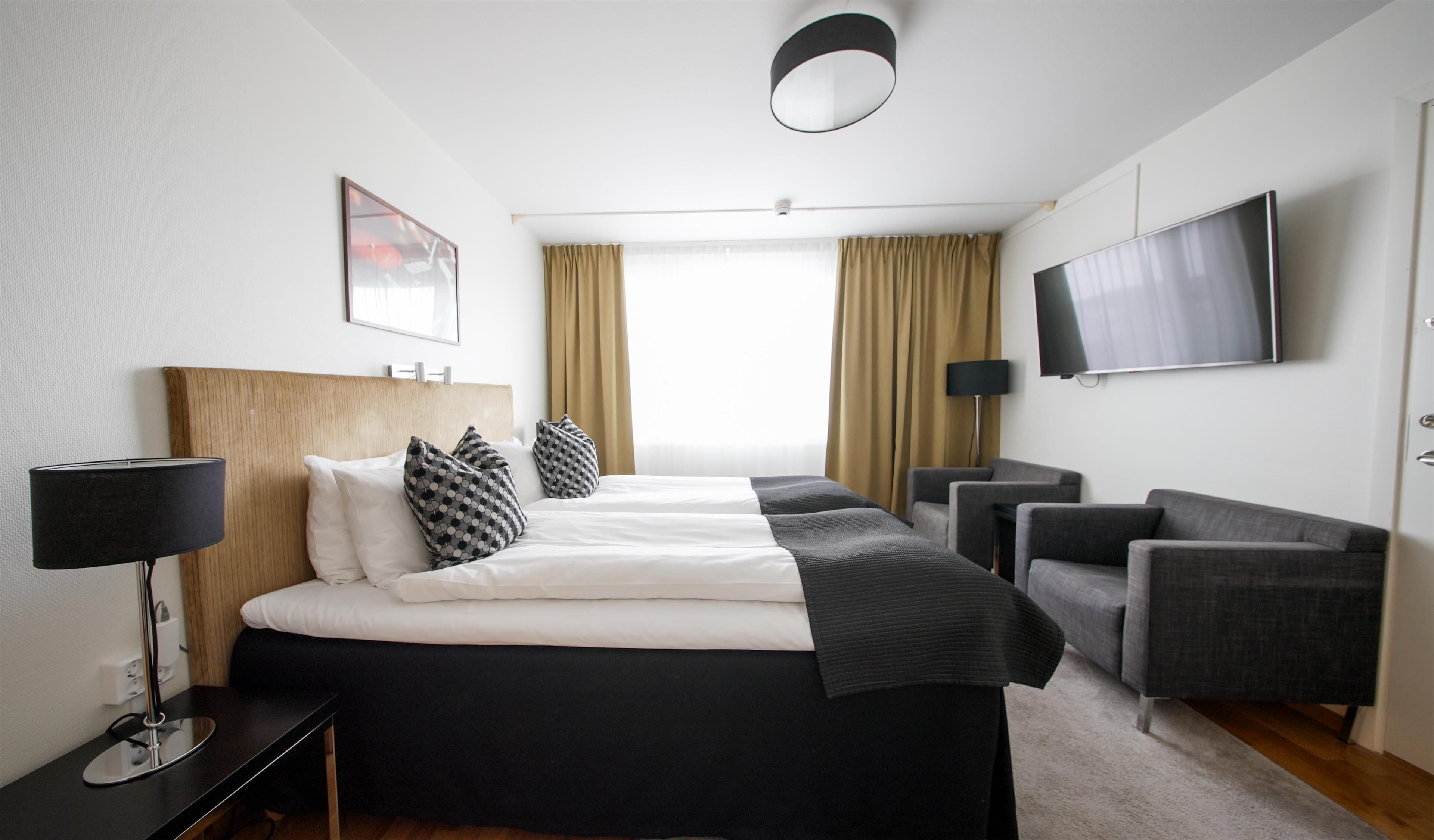 Ein Hotelzimmer mit einem großen Bett, zwei Nachttischen, einem Fernseher und einer Sitzecke mit Stühlen.