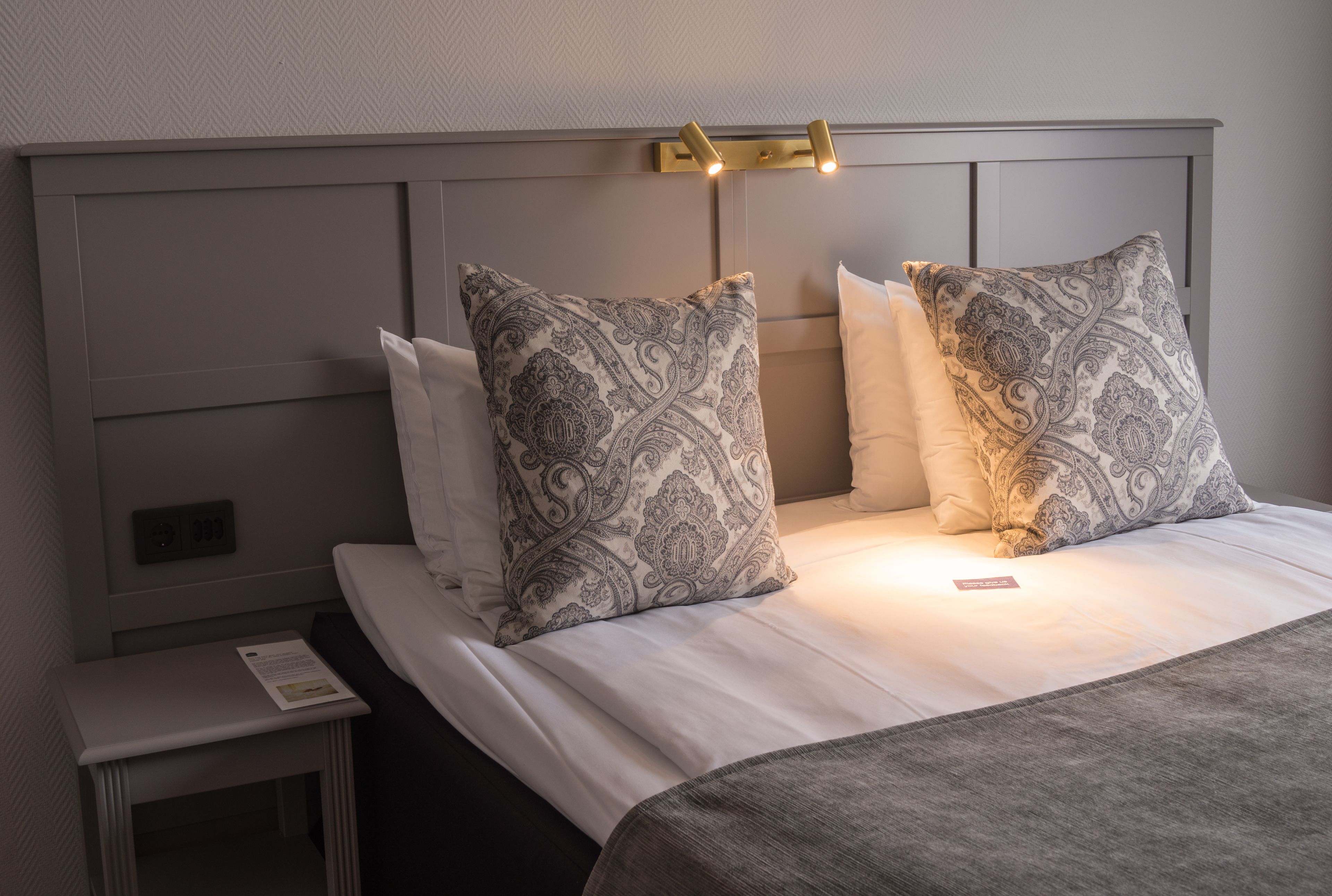 A neatly made bed with patterned pillows and a bedside table with a lamp.