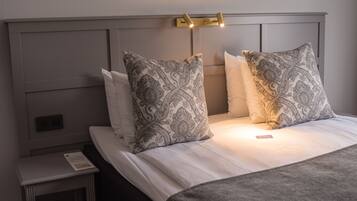 Una cama bien hecha con almohadas estampadas y una mesita de noche con una lámpara.