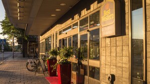 A building with a sign reading "Best Western" and large windows. There are potted plants outside and a bicycle parked on the sidewalk.