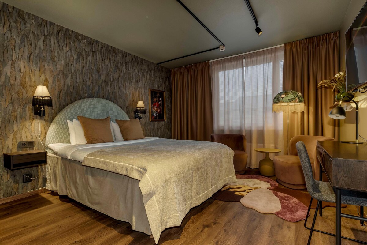 Un dormitorio moderno con una cama grande, lámparas de noche, una mesita pequeña, una silla y una alfombra decorativa.
