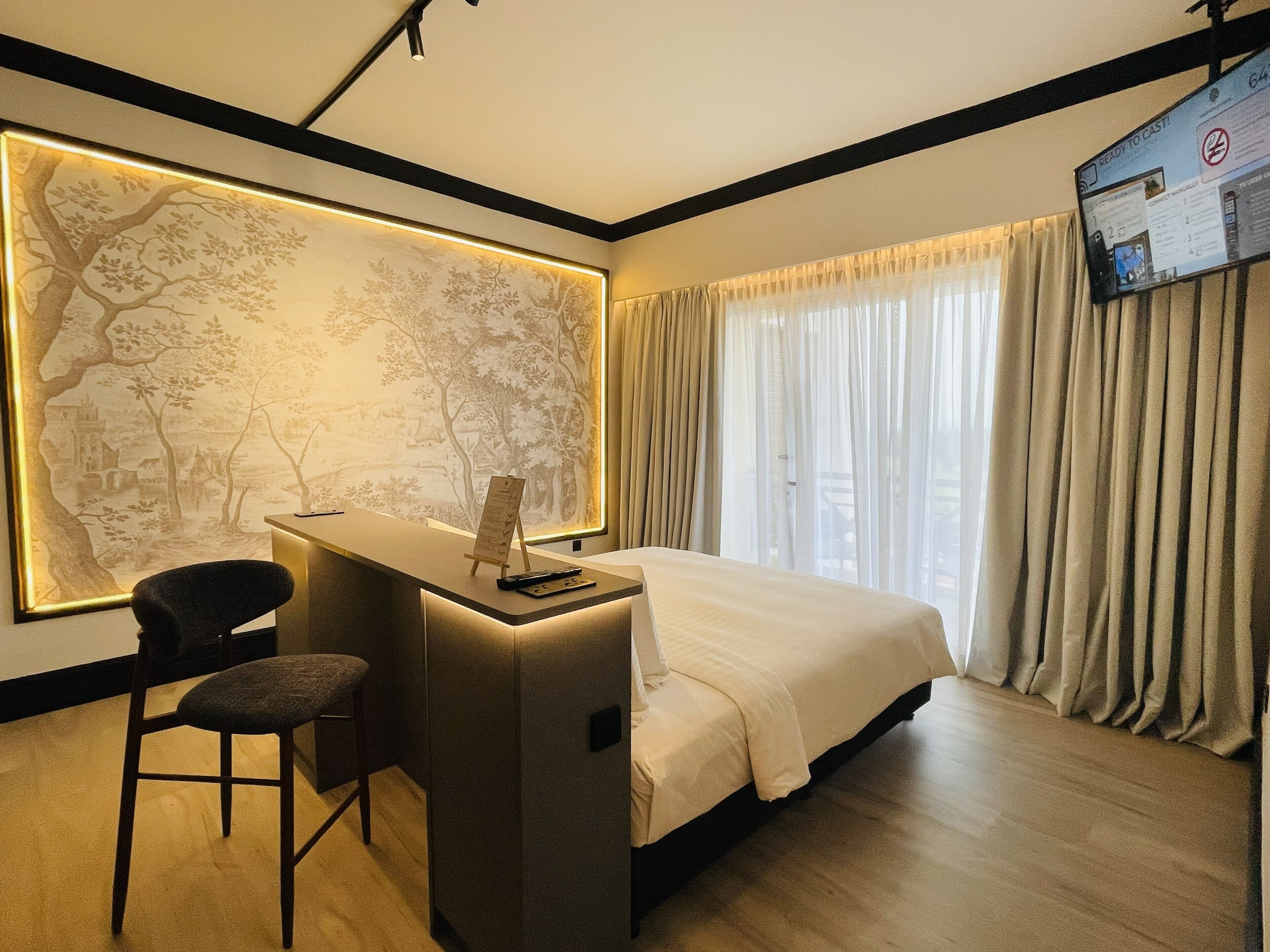 A hotel room with a desk, chair, bed, and a large wall mural.