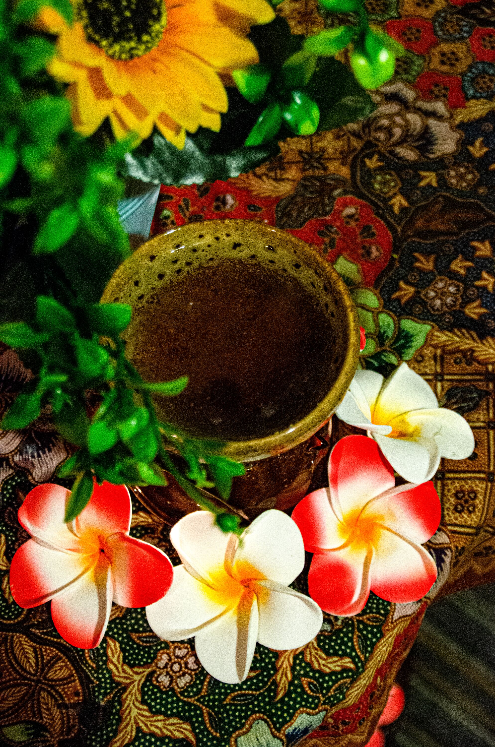 Un jarrón decorativo con un arreglo floral, que incluye flores de plumeria, sobre una superficie estampada.