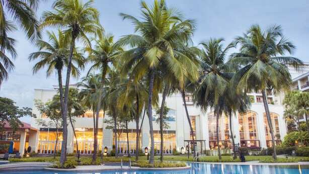 Un resort con piscina, palmeras y un edificio con amplios ventanales.