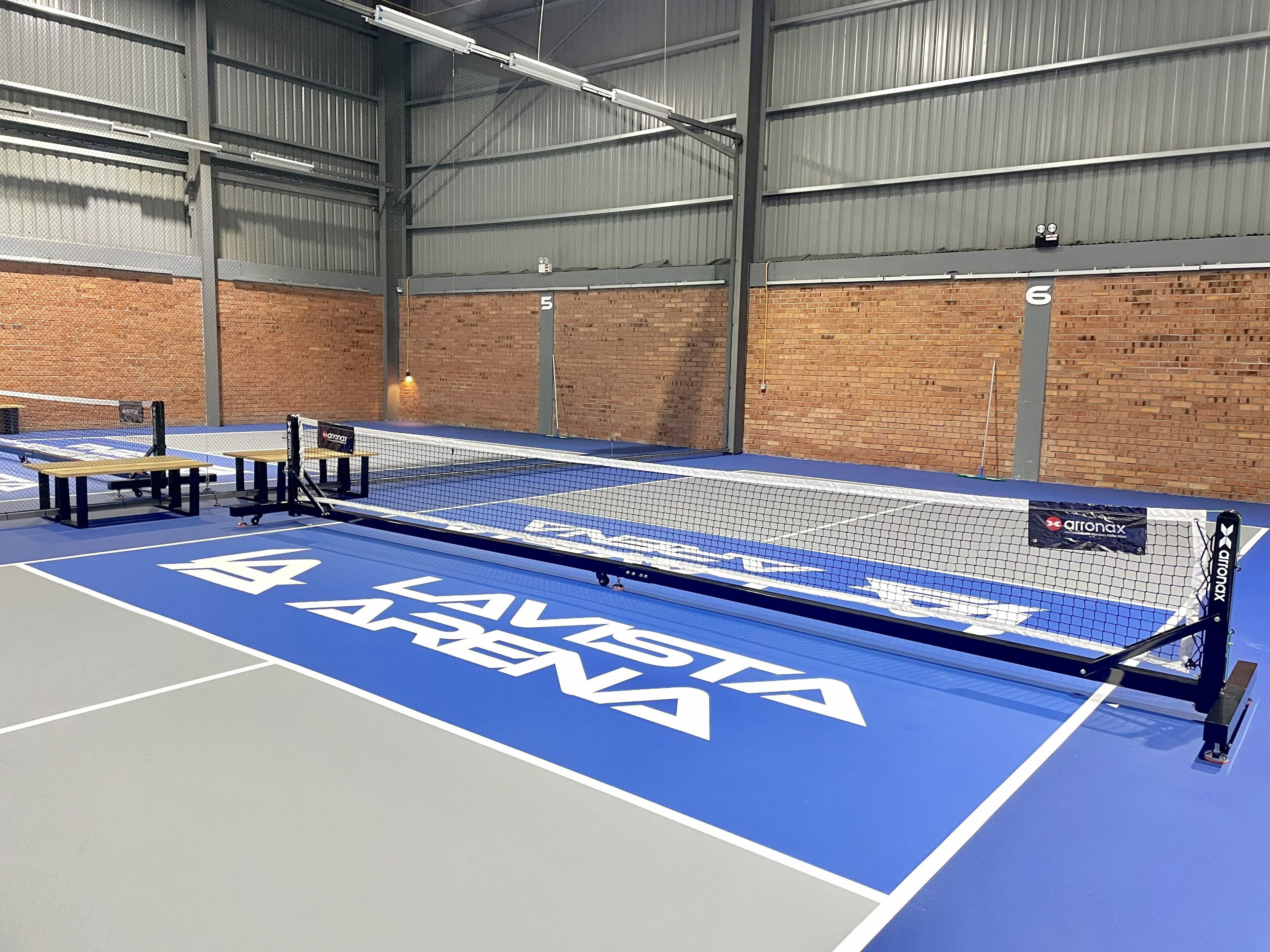 An indoor tennis court with a blue playing surface, white boundary lines, and a net.