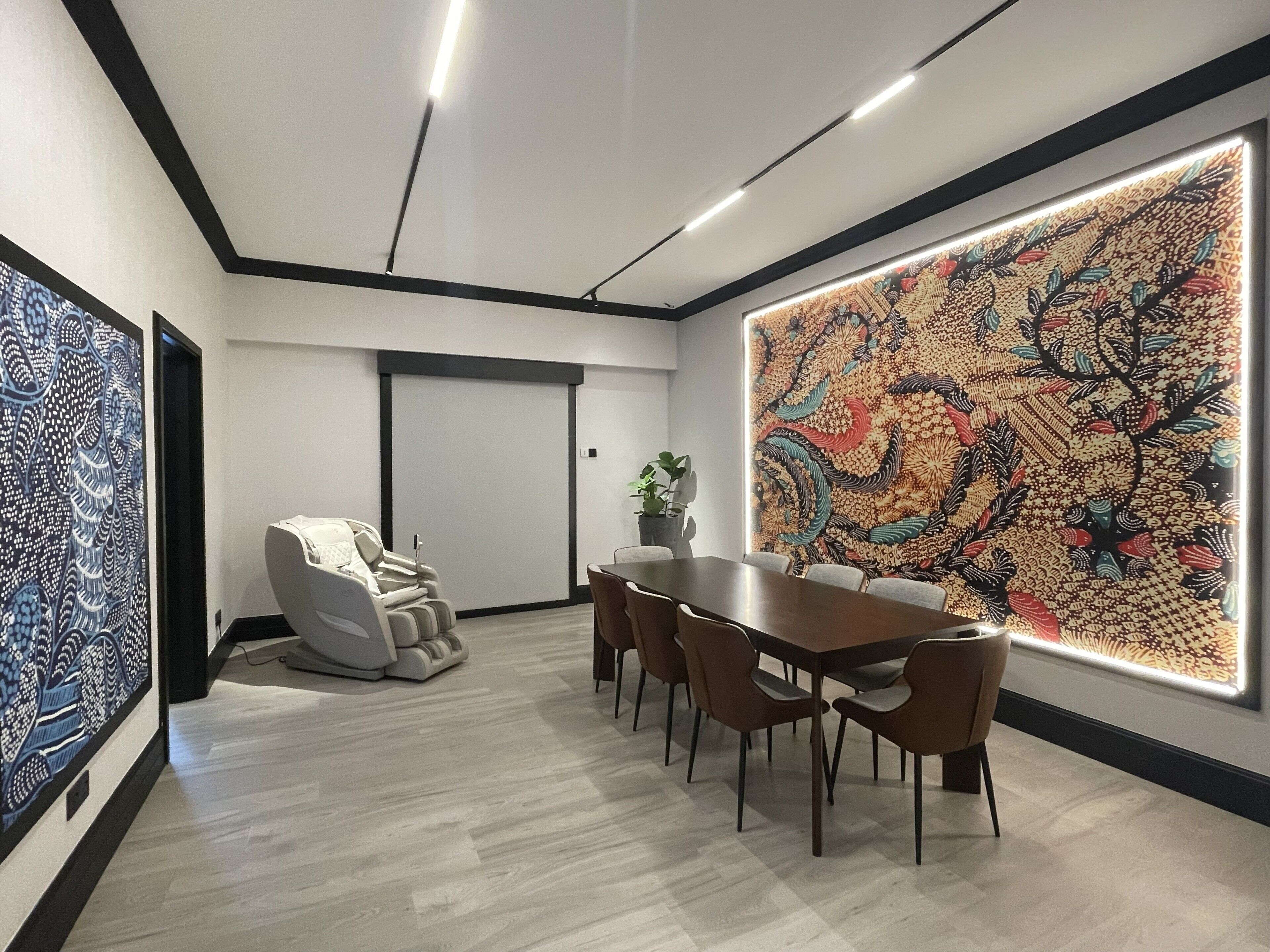 Una sala de conferencias con una mesa grande, sillas, un sillón de masajes y un cuadro abstracto y llamativo en la pared.