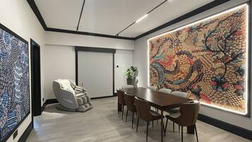 A conference room with a large table, chairs, a massage chair, and a vibrant abstract painting on the wall.