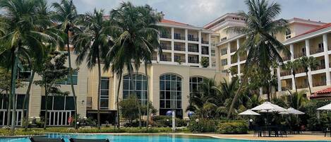 A hotel with a swimming pool, palm trees, and a multi-story building with balconies.