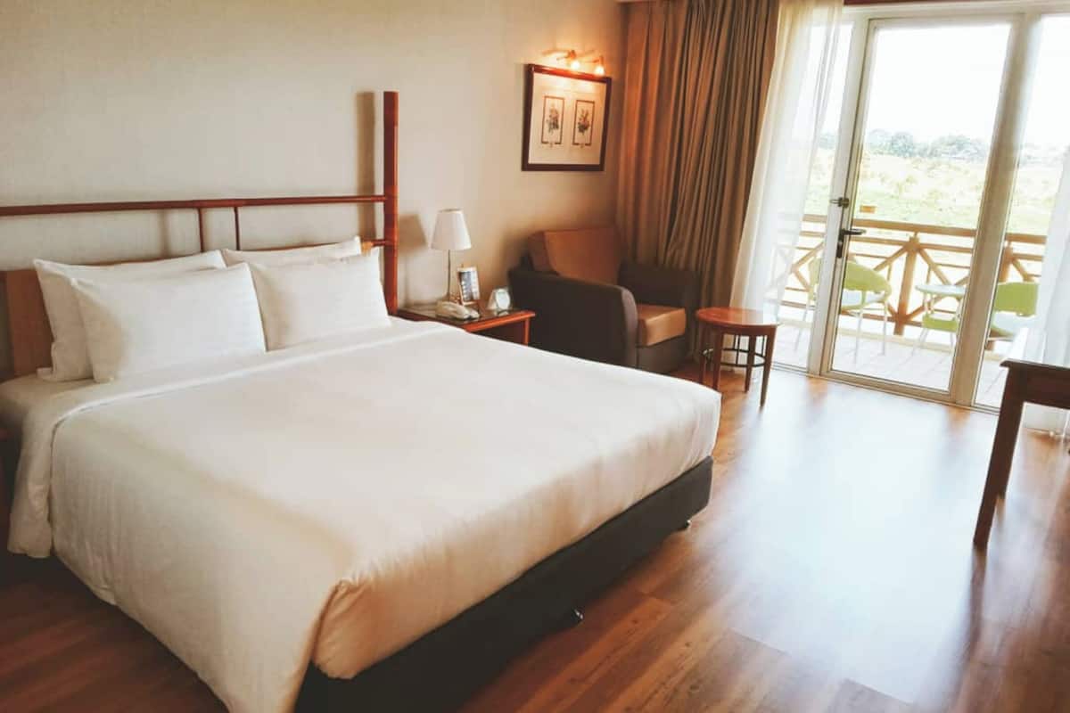 A hotel room with a large bed, a chair, a small table, a lamp, and a view of the outdoors through a sliding door.