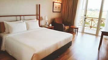 A hotel room with a large bed, a chair, a small table, a lamp, and a view of the outdoors through a sliding door.