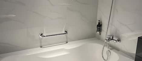 Un baño moderno con una bañera independiente, un cabezal de ducha de mano y un perchero para toallas.