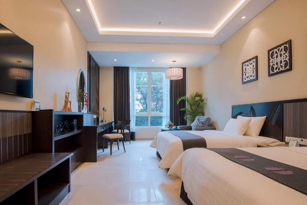 A modern hotel room with two beds, a desk, a TV, and a large window.