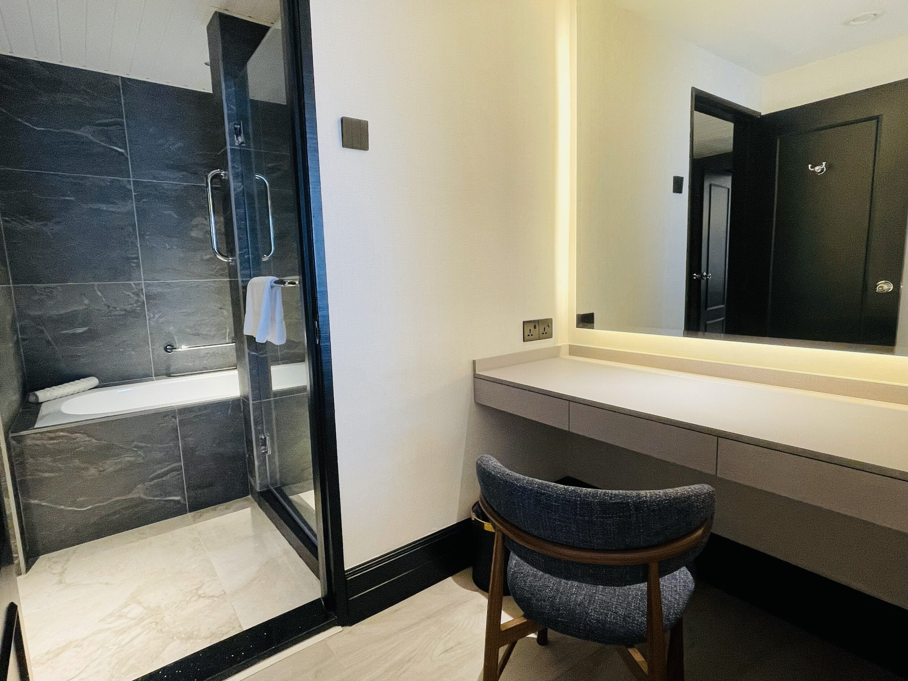 A modern bathroom with a glass shower enclosure, a white bathtub, and a vanity with a mirror.