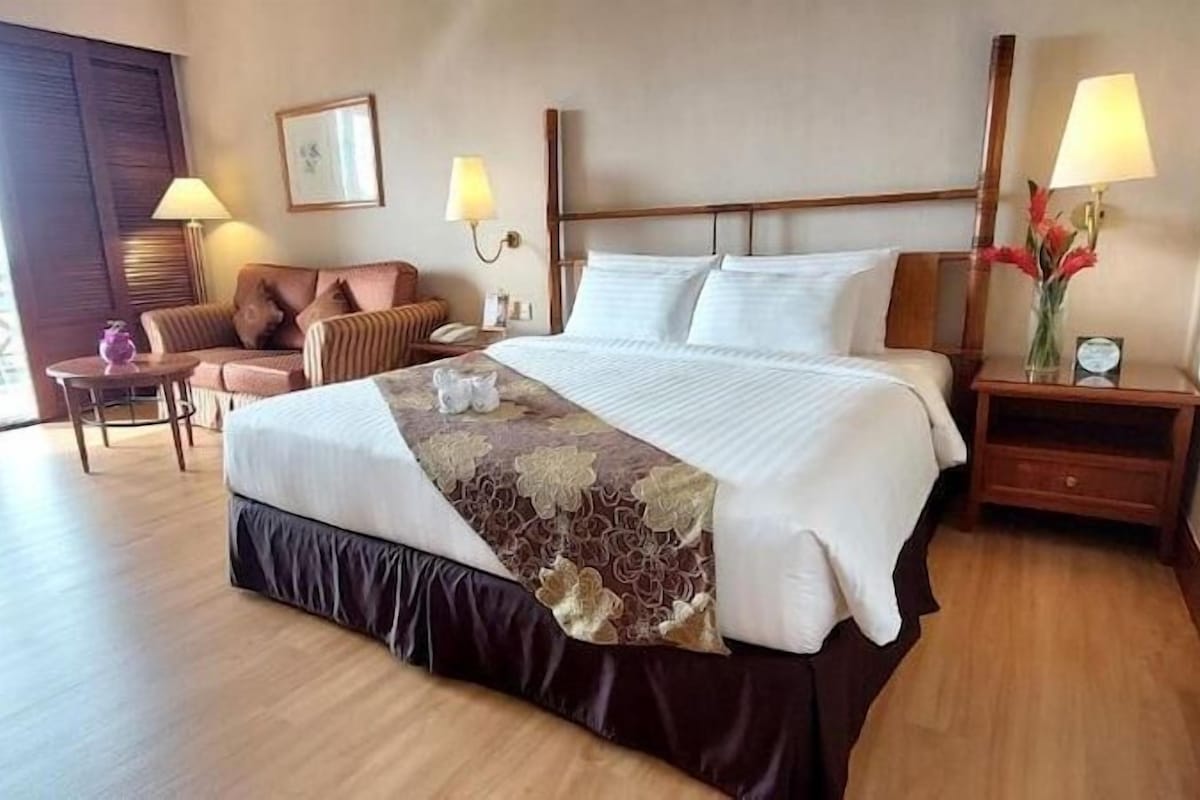 A hotel room with a bed, a chair, a nightstand, a lamp, and a view of the outdoors.